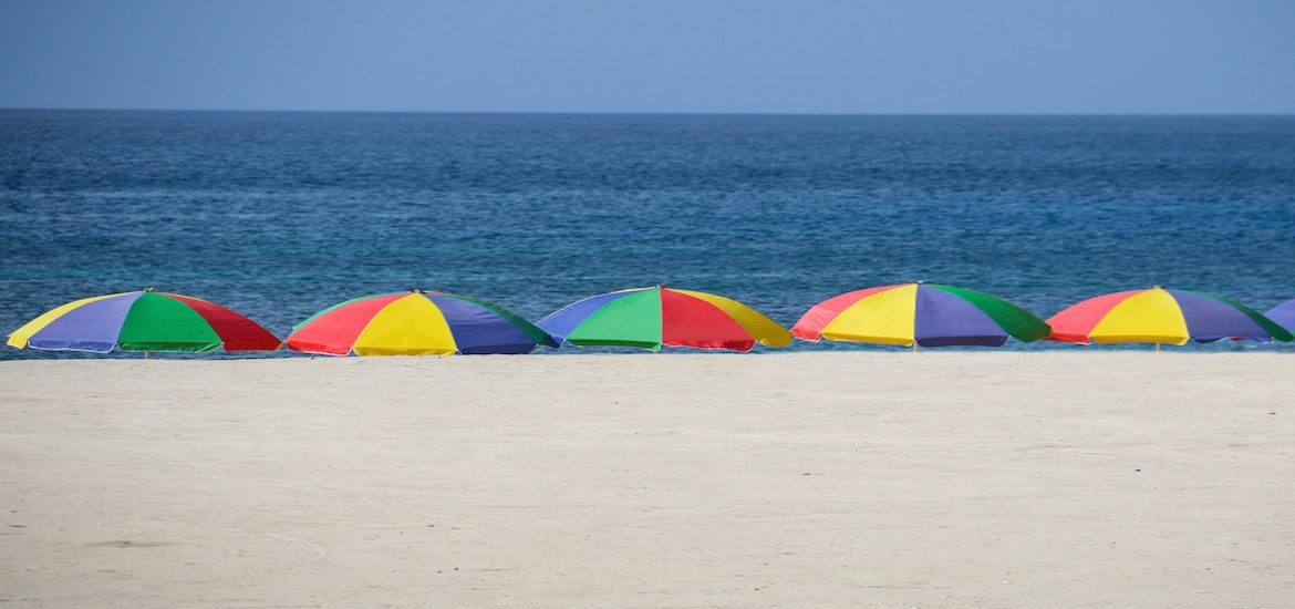 Beach scene with five umbrellas staked in the sand, each multi-colored.