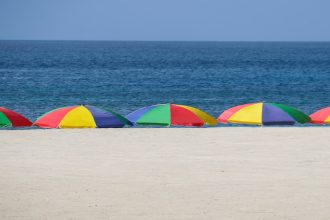 Beach scene with five umbrellas staked in the sand, each multi-colored.