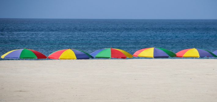 Beach scene with five umbrellas staked in the sand, each multi-colored.