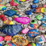 Colorful rock on rocky shore. One rock with word kindness stands out/
